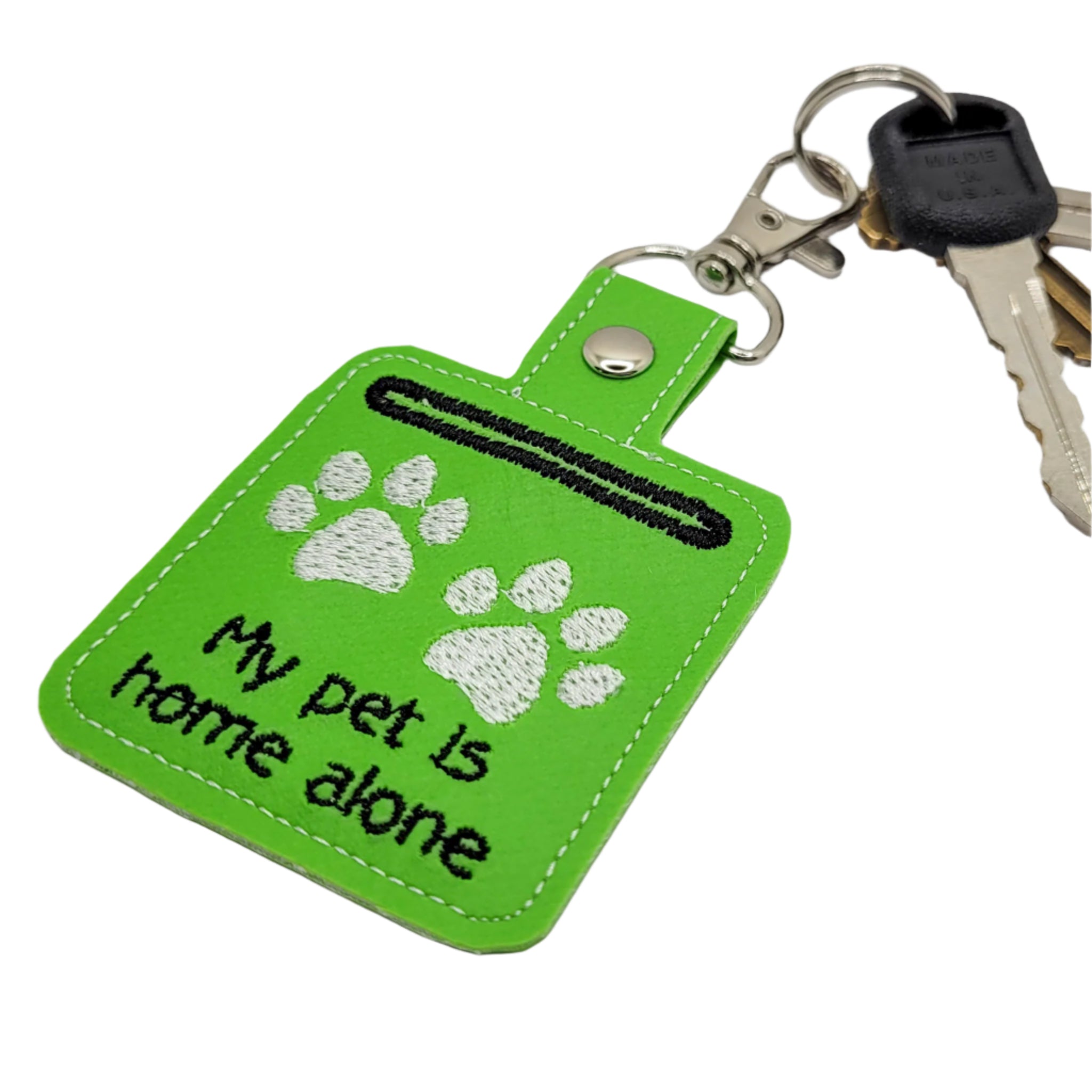 Green keychain with paw prints and text 'My pet is home alone' on a light gray background