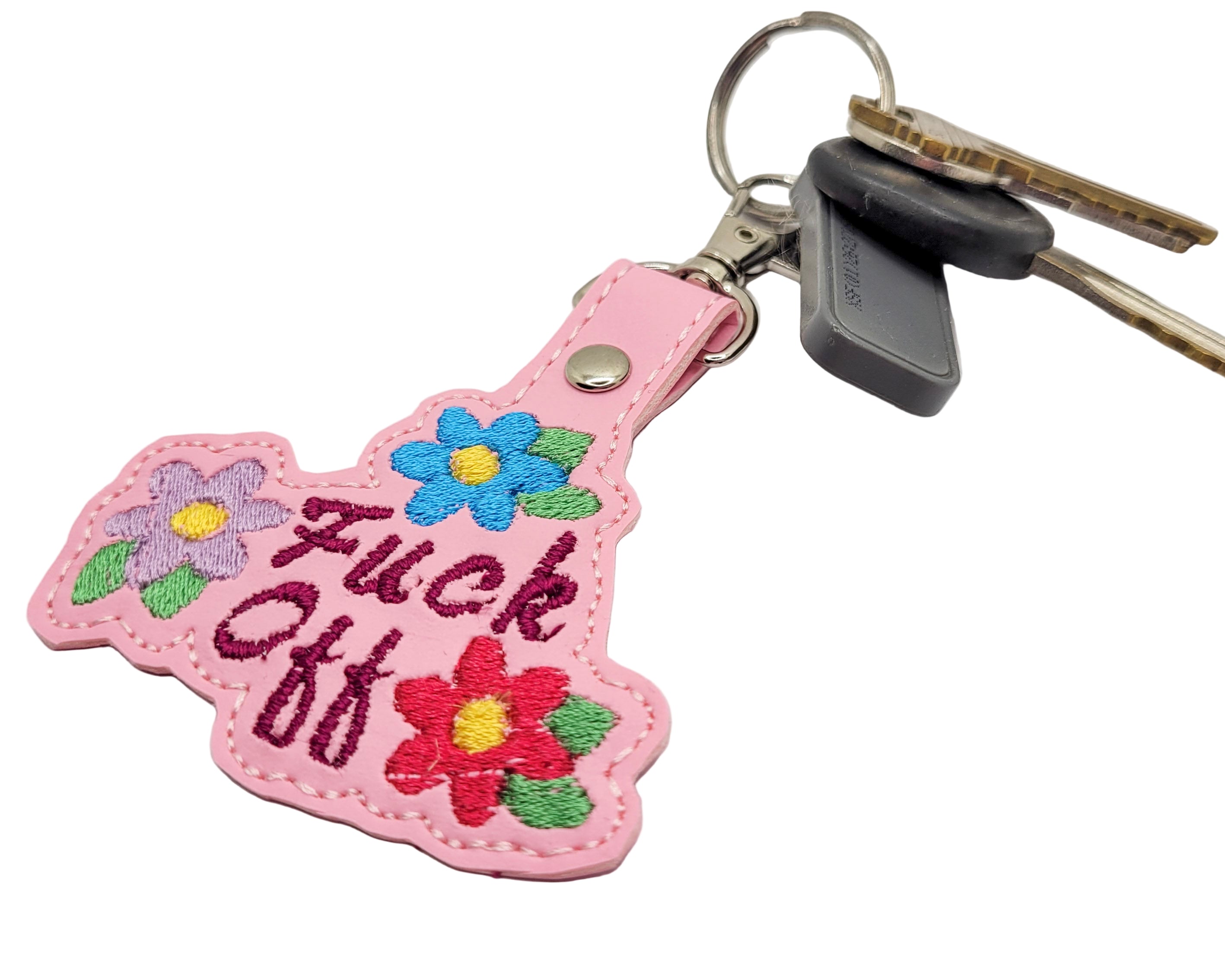 Pink keychain with floral designs and text on a marble surface