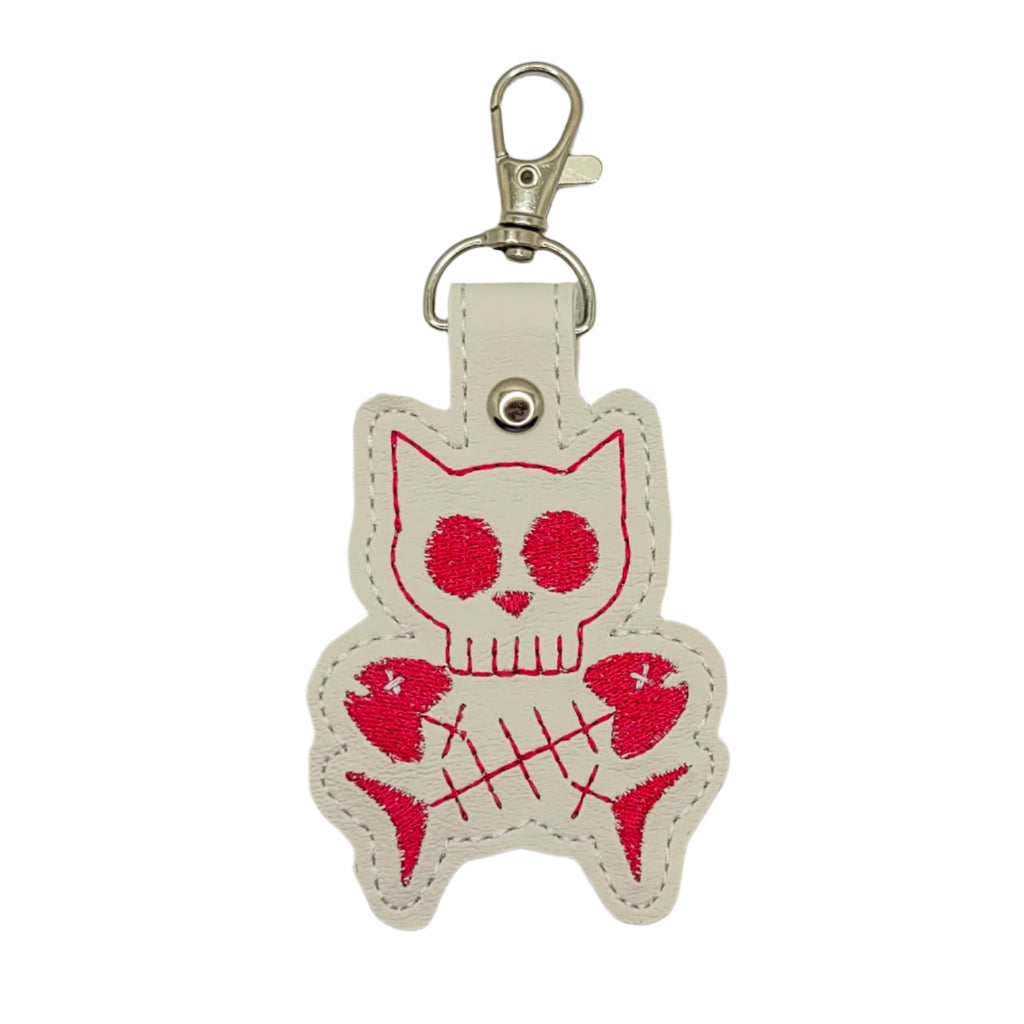 Cat-shaped keychain with skull design on a gray background