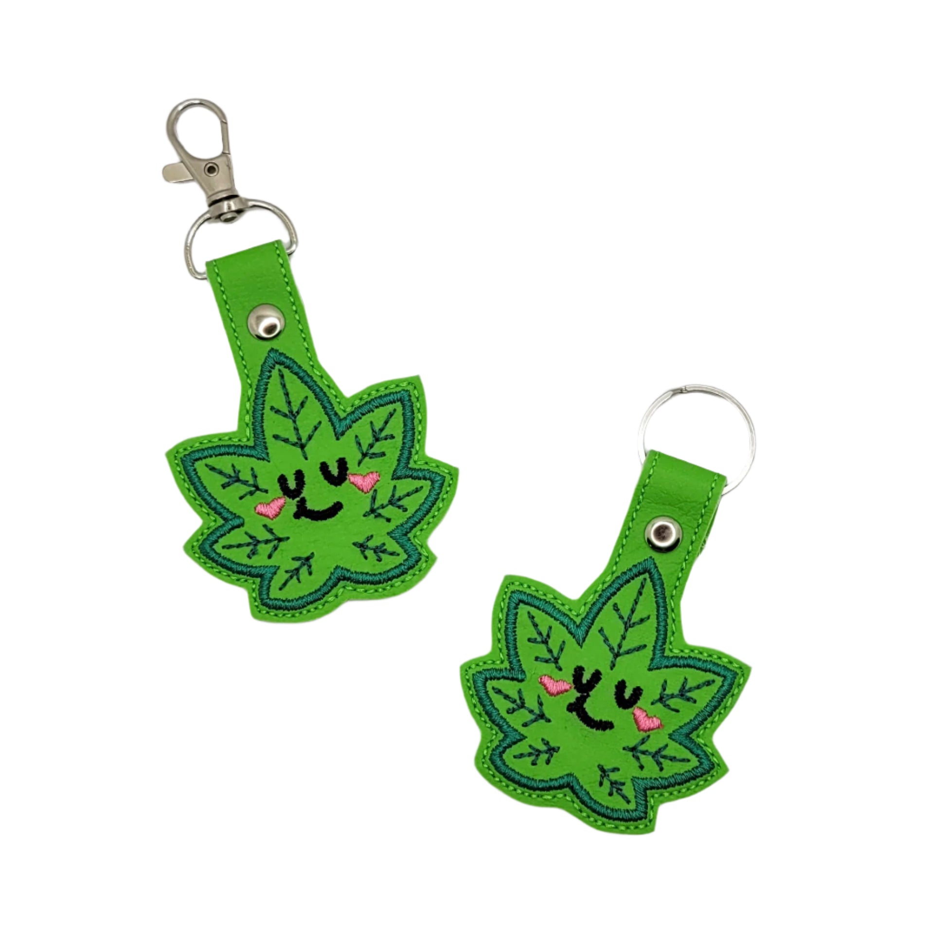 Two green leaf-shaped keychains with smiling faces on a gray background