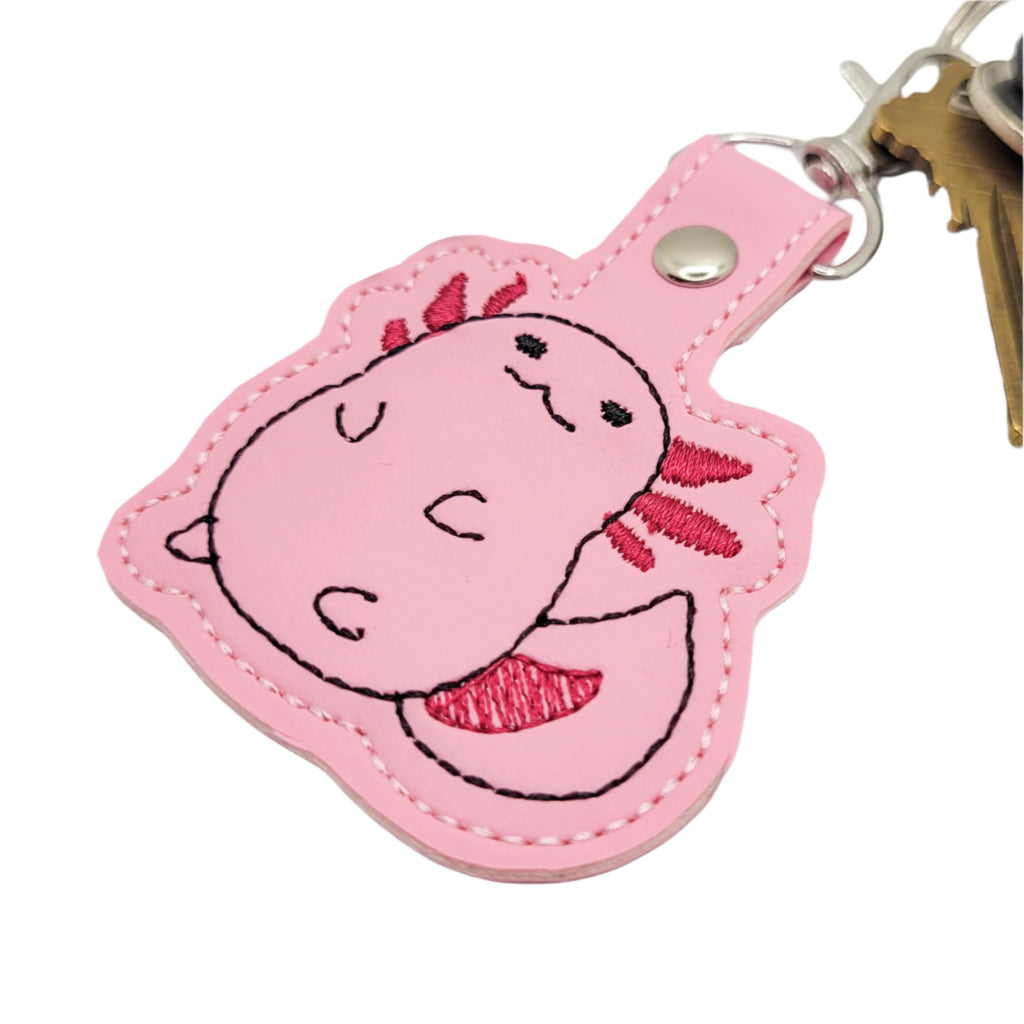 Embroidered vinyl keychain featuring a pink chubby axolotl with dark pink gills, attached to a set of keys