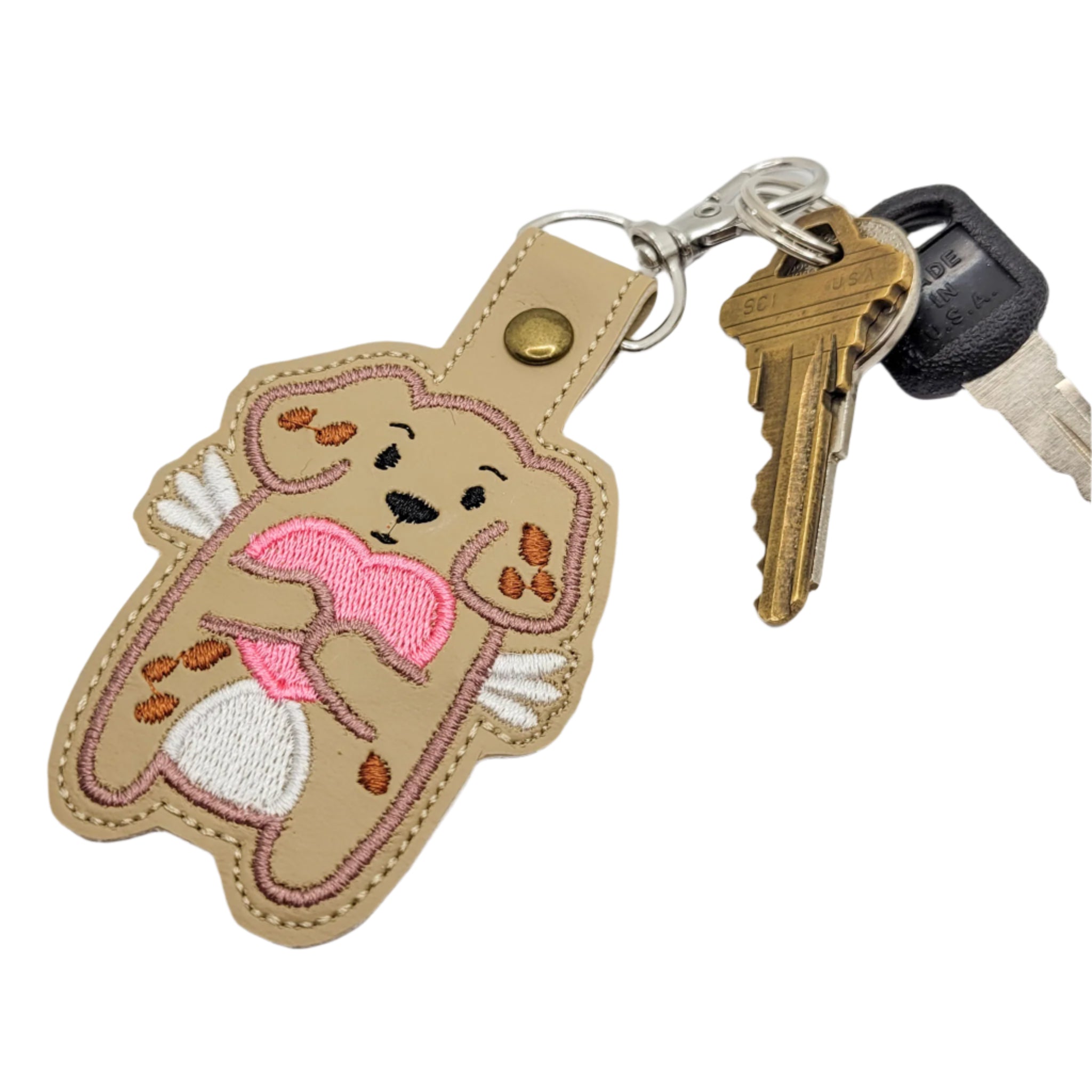 Embroidered vinyl keychain featuring a cartoon dog with white wings holding a pink heart, attached to a set of keys
