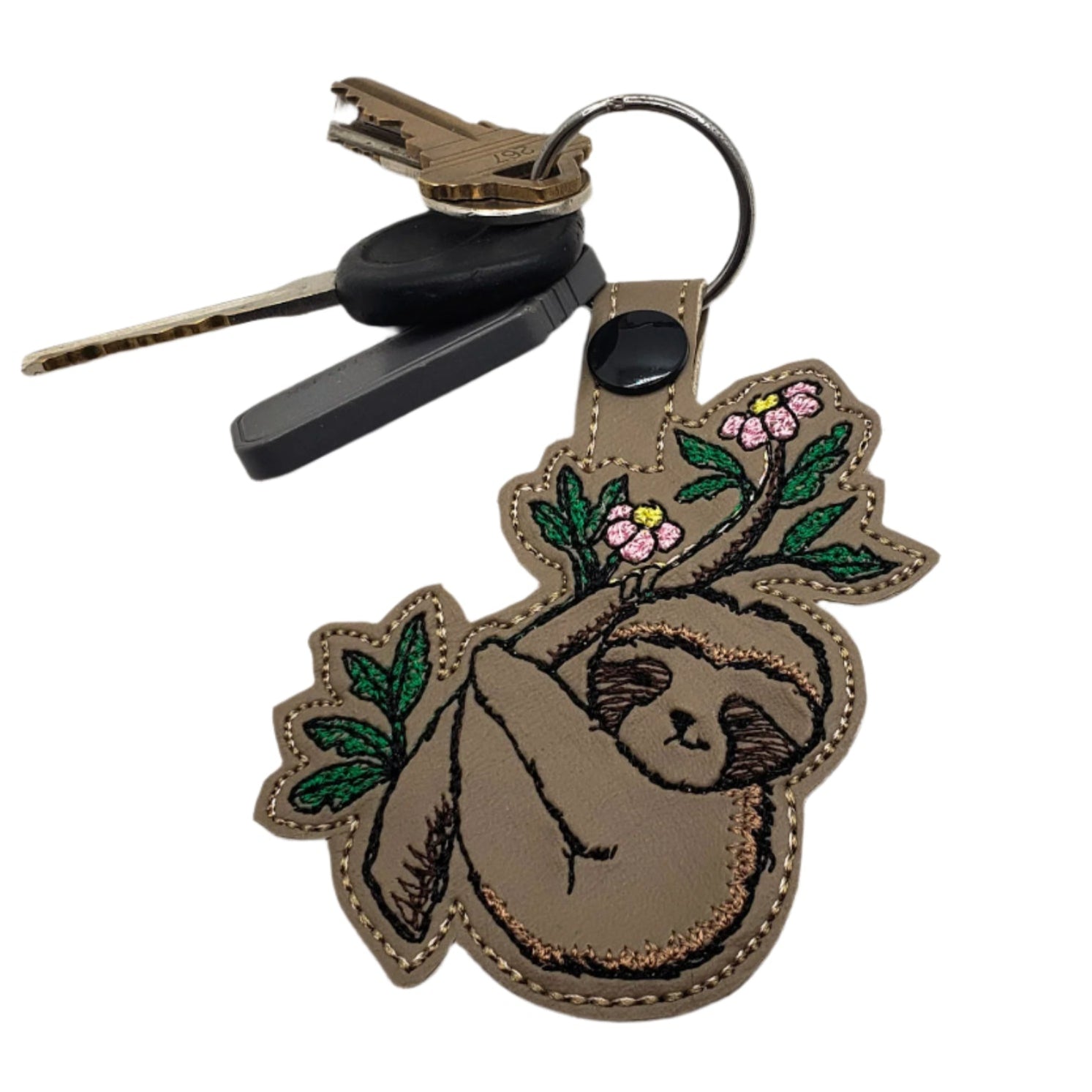 Embroidered vinyl keychain featuring a sloth hanging in a flowering tree, attached to a set of keys