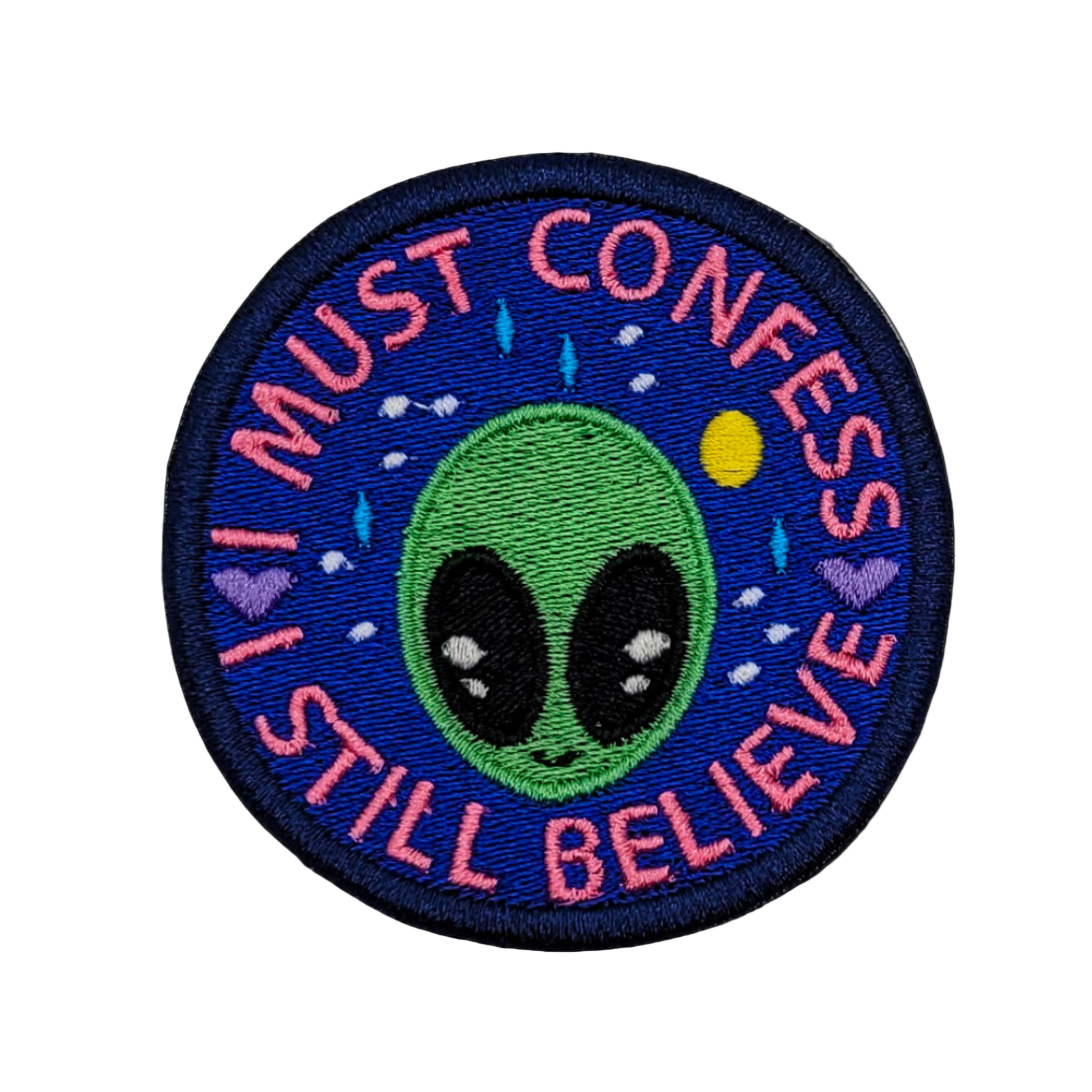 This image features an embroidered patch with the phrase "I Must Confess I Still Believe" alongside a depiction of an alien. The design includes a green alien face with large, expressive eyes set against a cosmic backdrop, complete with stars and planets.