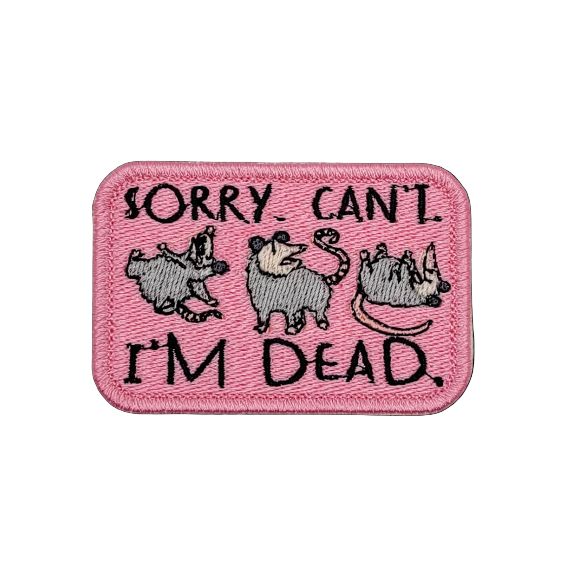 A pink embroidered patch with the text 'Sorry. Can't. I'm Dead.' and three possum illustrations.