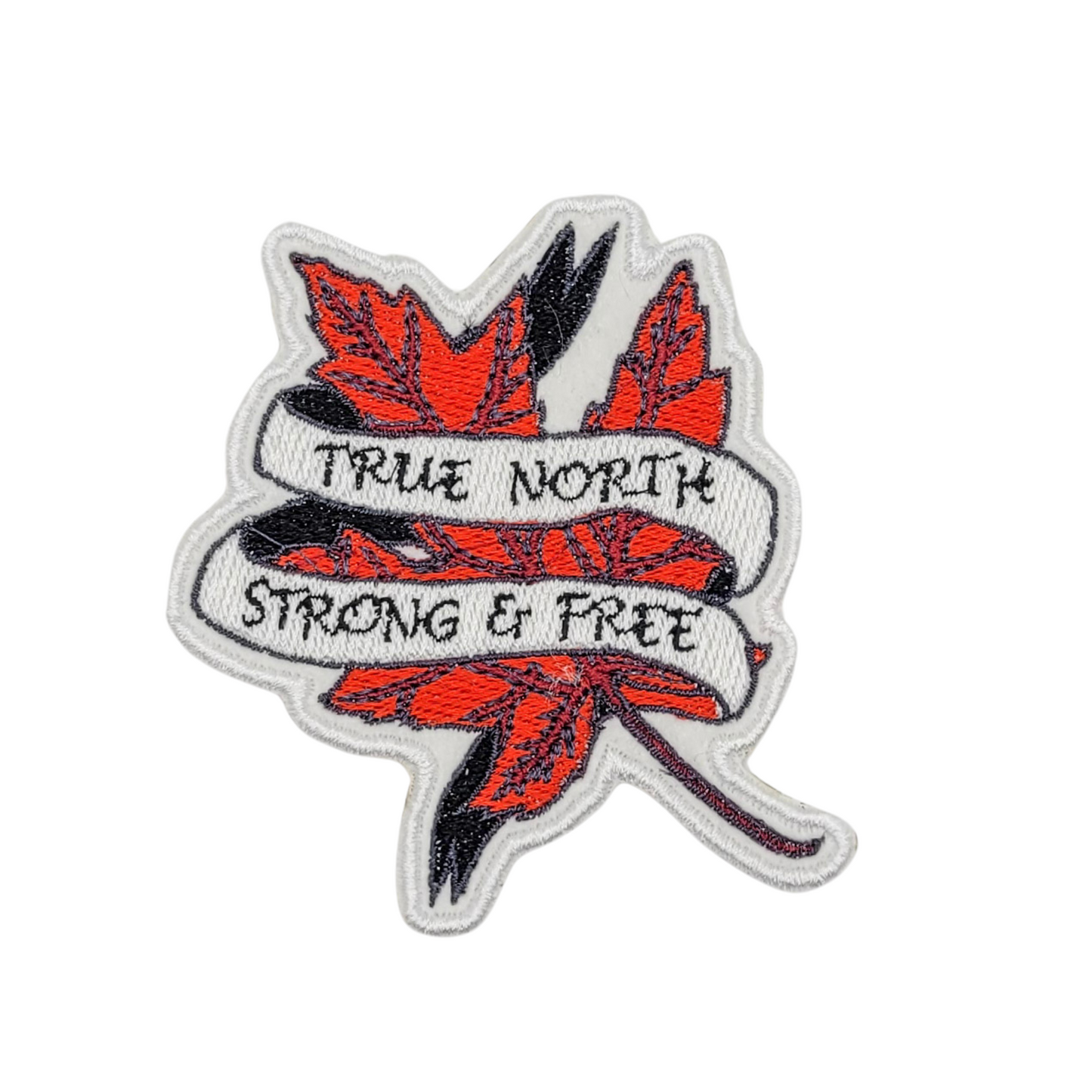 Close-up of the True North Strong & Free patch on a white background. The detailed embroidery showcases bright red maple leaves with black outlines and a flowing white banner with bold black text. The patch has a clean, white embroidered border.