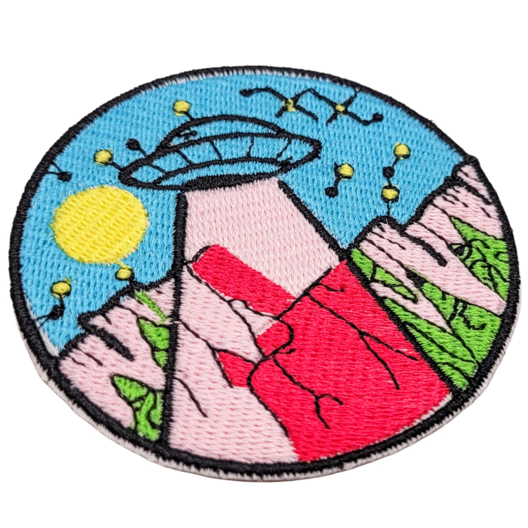 Embroidered patch with a colorful design of a ufo, mountains, and sun. 