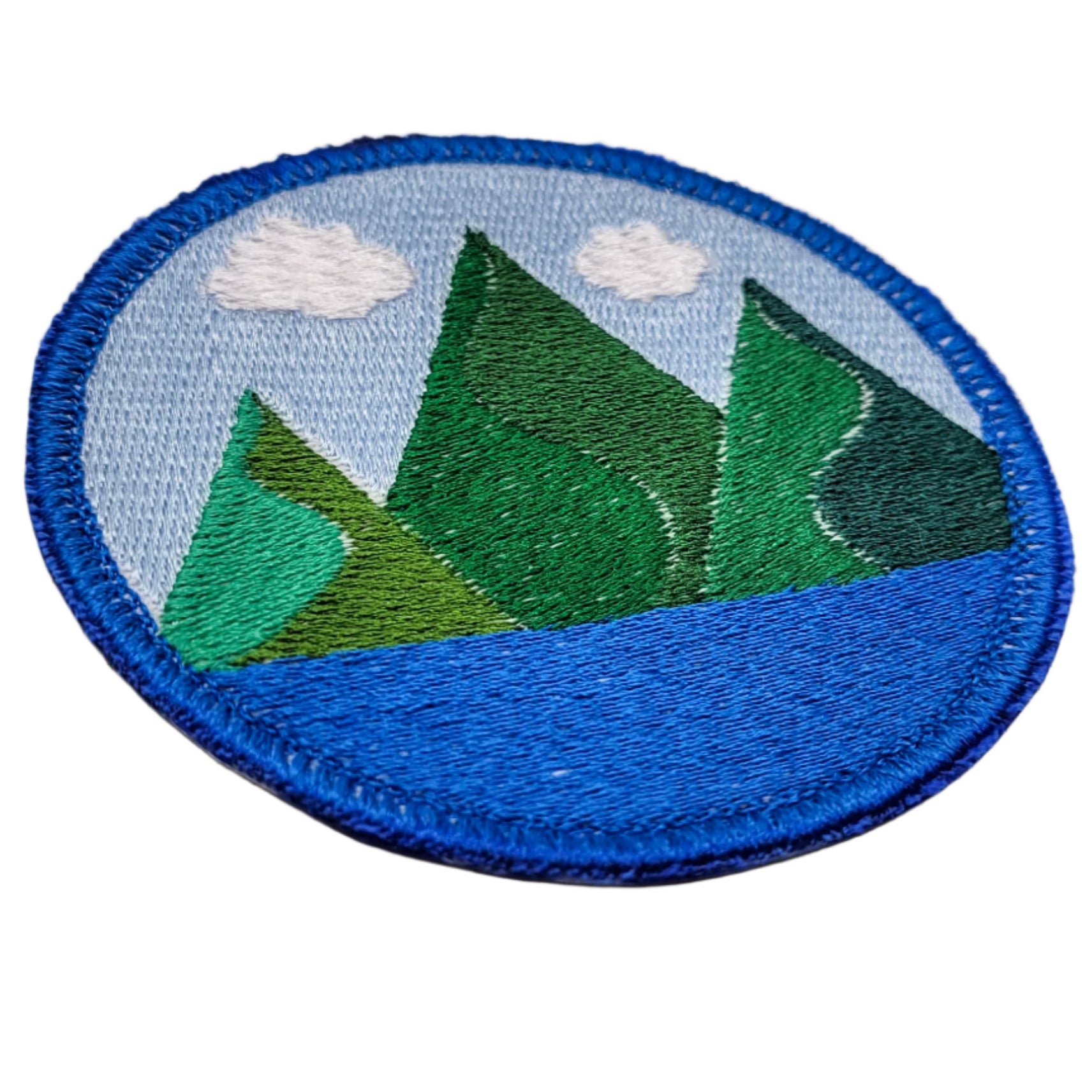 Circular patch with embroidered mountains and blue sky on a white background.